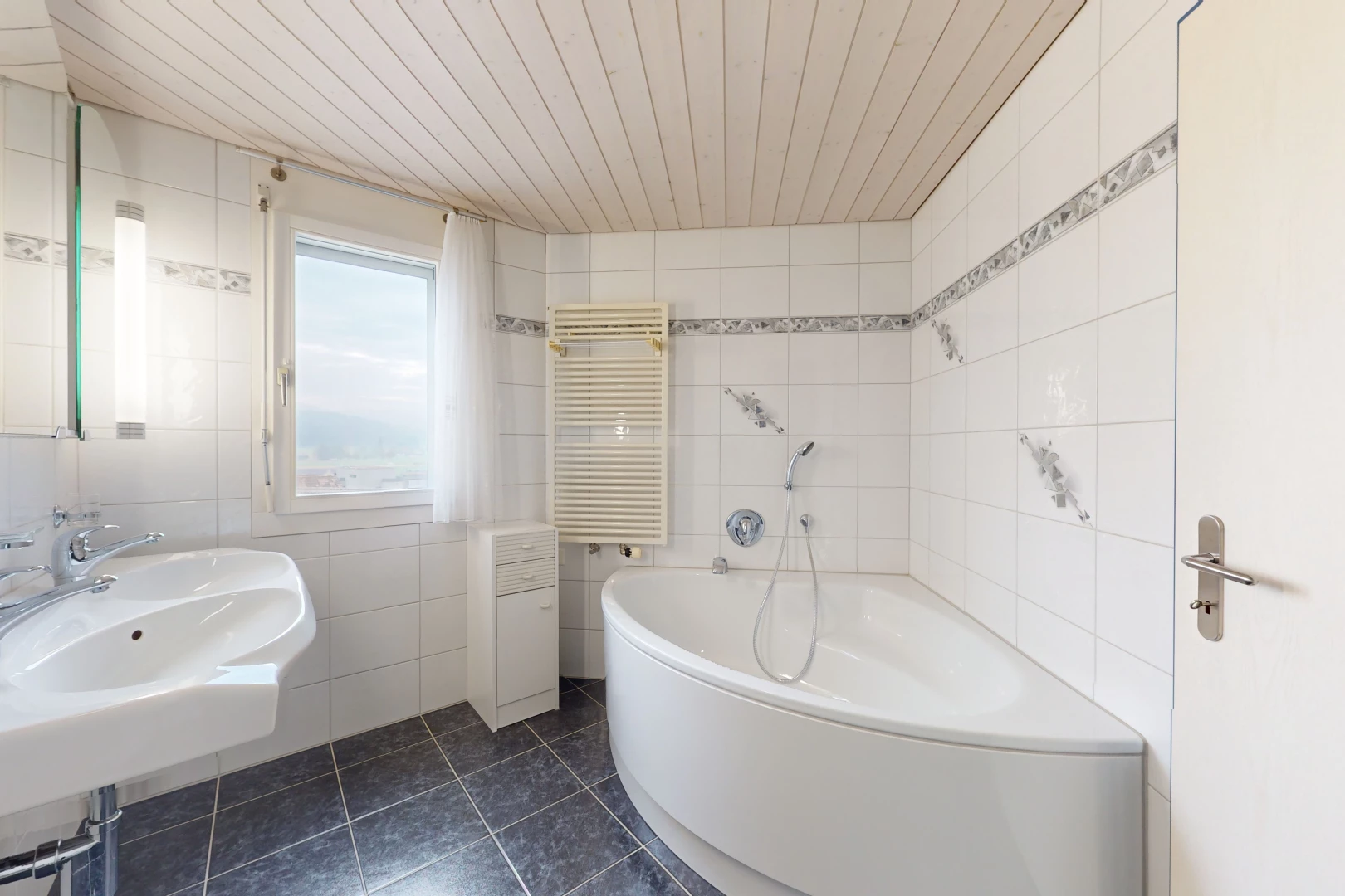 salle de bain avec radiateur, lumière naturelle, vasque, mur carrelé, et plafond de bois