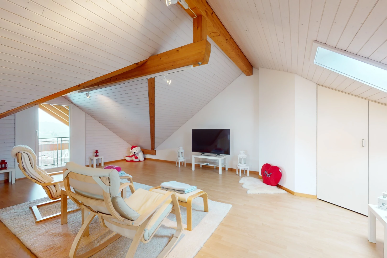 espace intérieur avec poutres apparentes, télévision, plancher de bois, plafond voûté, et éclairage sur rail