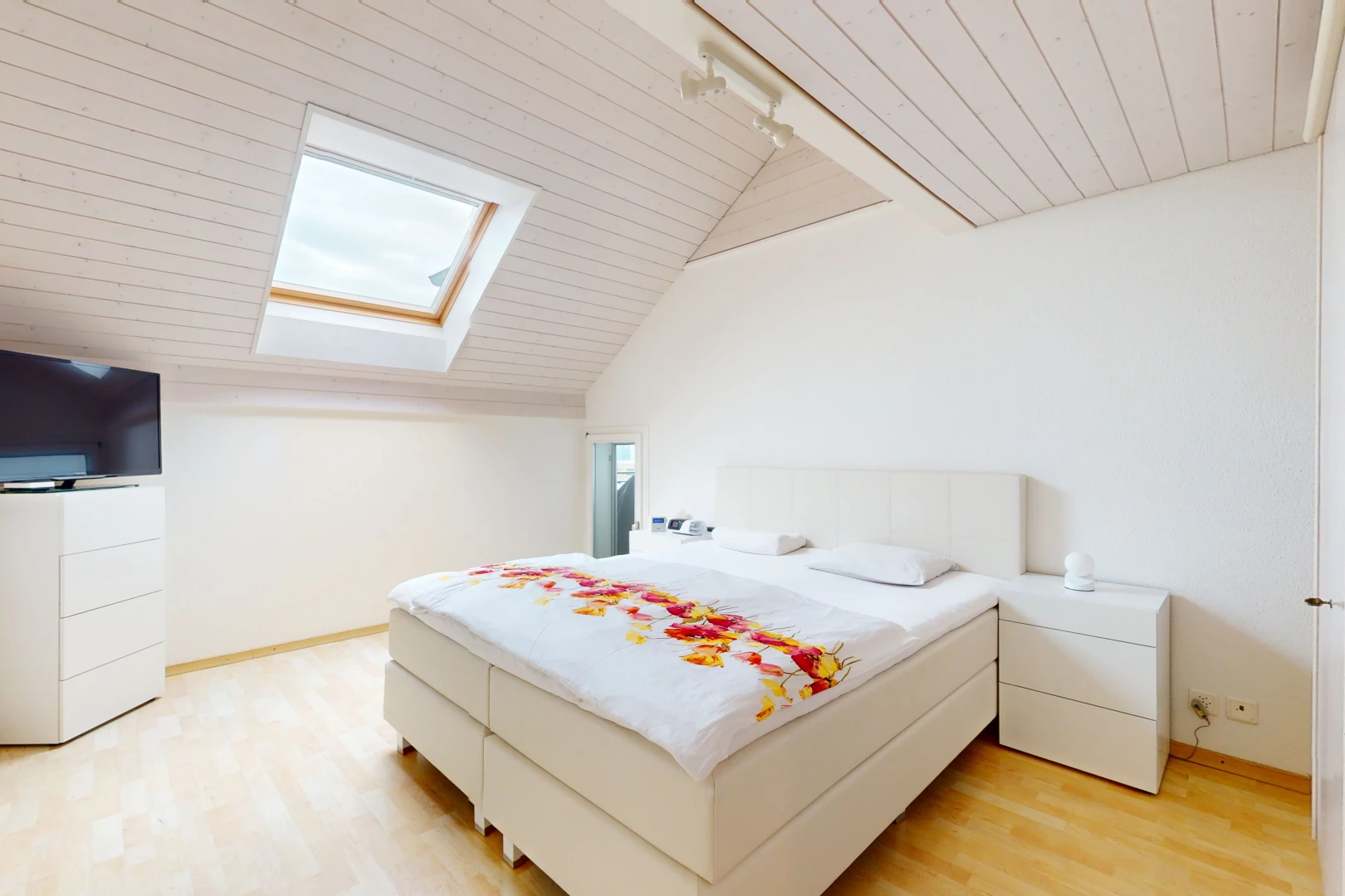 chambre avec télévision, plancher de bois, lucarne, plafond voûté, et éclairage sur rail