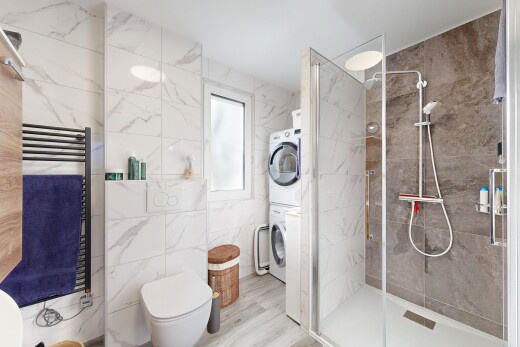 bathroom with a towel warming rack, tile walls, radiator heating unit, a stall shower, and stacked washer / drying machine