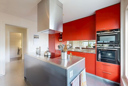 küche mit rote schränke, doppel backofen, dunstabzugshaube, edelstahl-arbeitsplatten, und schränke mit flachen paneelen