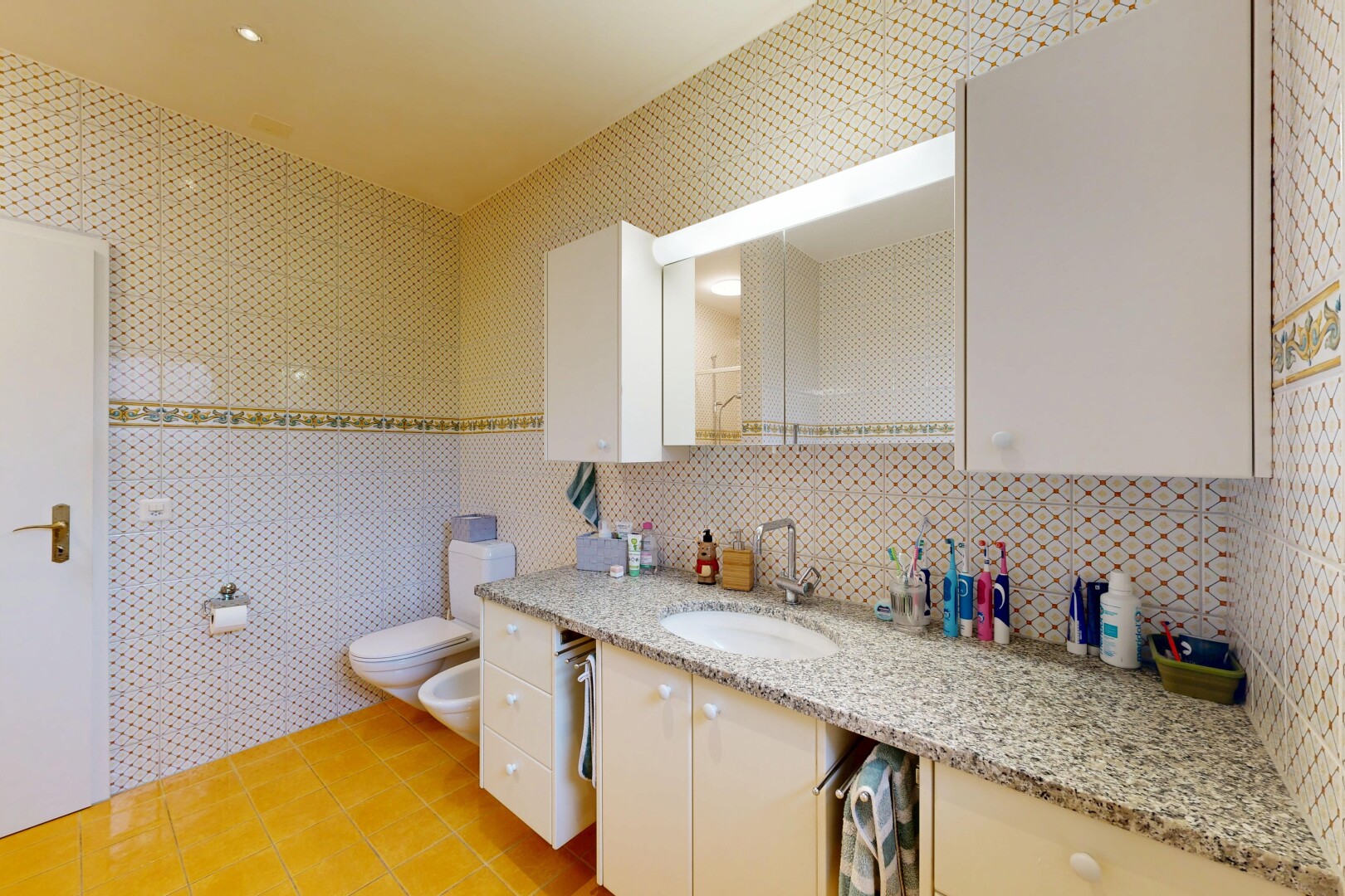 salle de bains avec sol en carrelage, tile floor, lavabo (ou coiffeuse selon le contexte), bidet, et miroir
