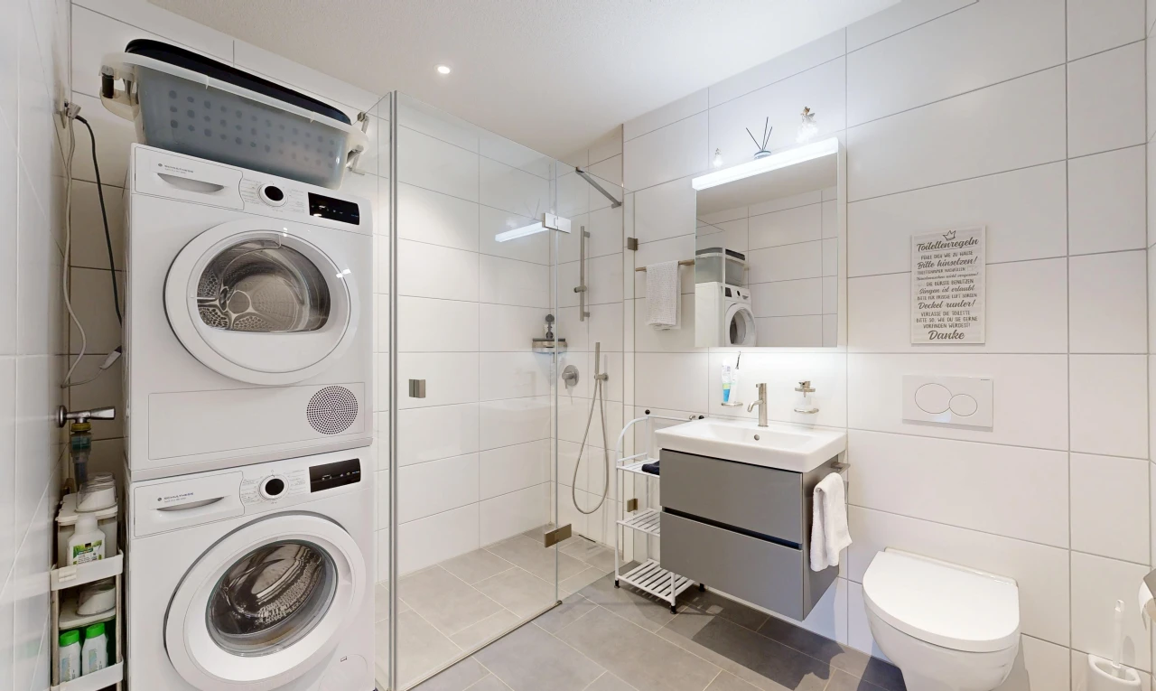 salle de bains avec lave-linge et sèche-linge superposés, douche, salle de bain complète, miroir, et lavabo (ou coiffeuse selon le contexte)