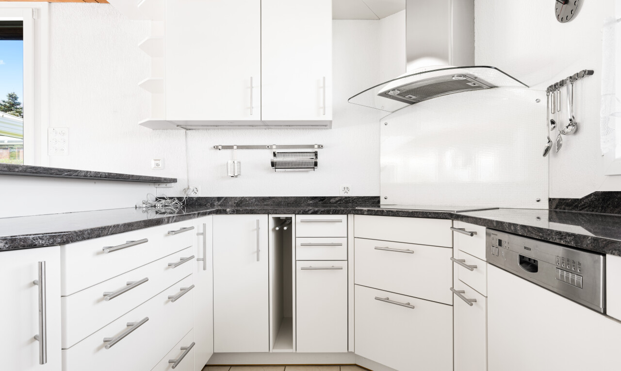 cuisine avec dark countertops, two heights countertops, hotte, armoires blanches, et white cabinets