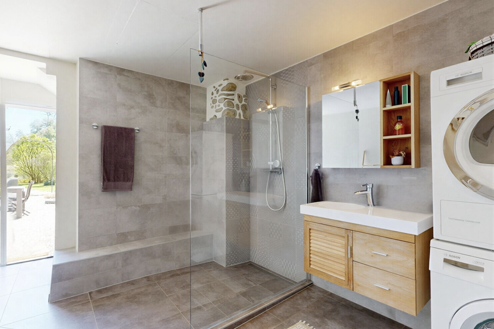 salle de bains avec salle de bain complète, lave-linge et sèche-linge superposés, douche, miroir, et lumière naturelle