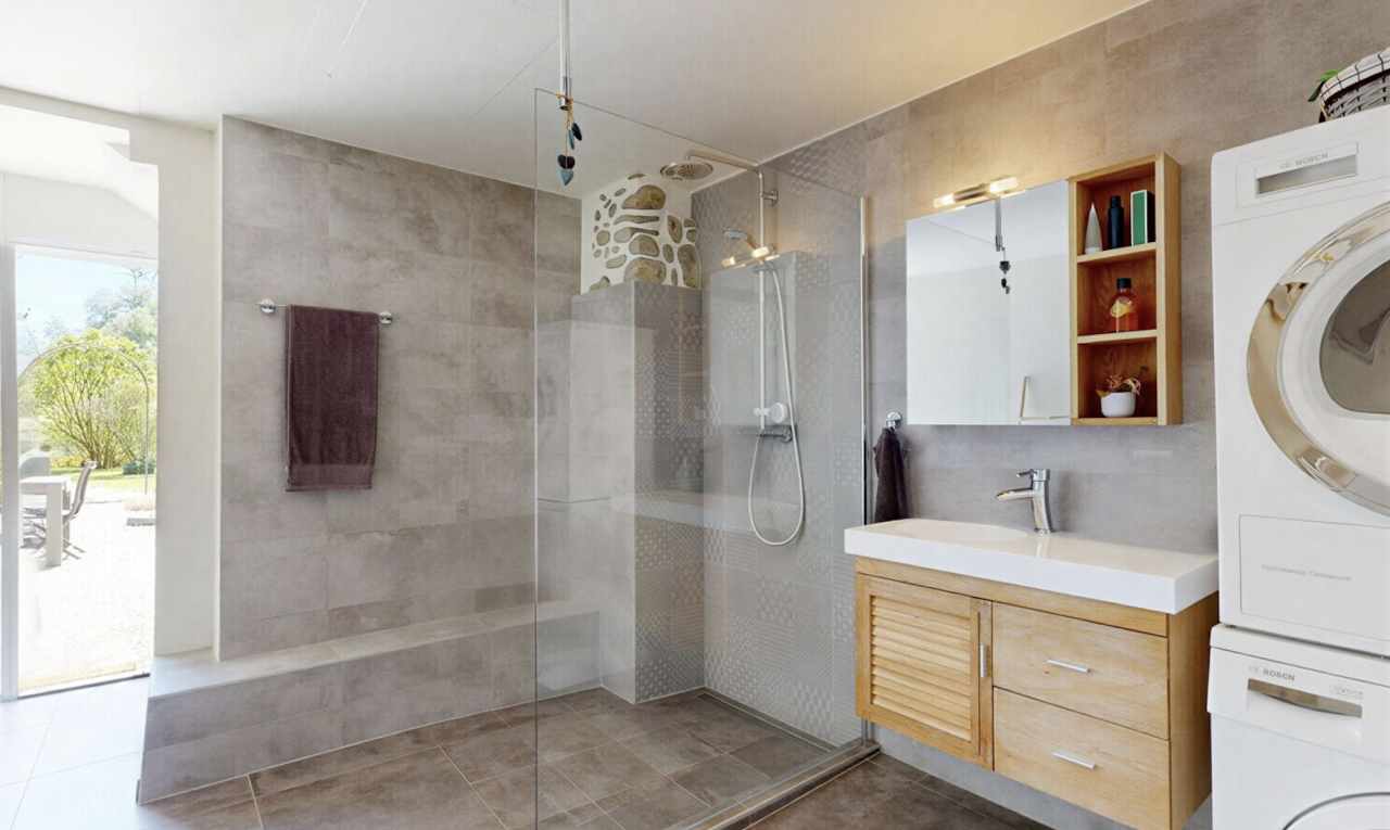 salle de bains avec salle de bain complète, lave-linge et sèche-linge superposés, douche, miroir, et lumière naturelle