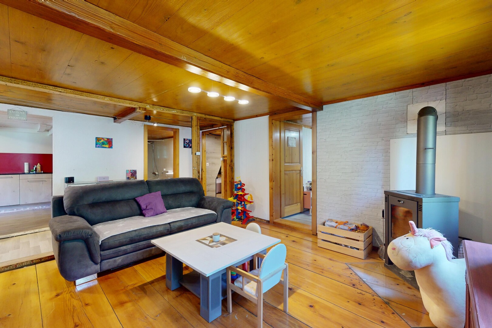 living area with a wooden ceiling with exposed beams, light wood finished floors, a wood stove, and brick wall