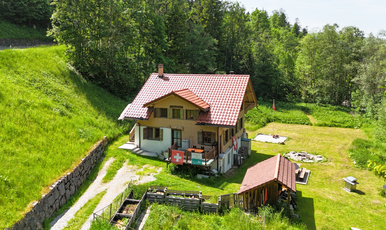 outdoor house featuring a tiled roof, a chimney, driveway, and a view of trees