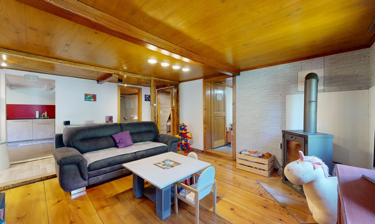 living area with a wooden ceiling with exposed beams, light wood finished floors, a wood stove, and brick wall