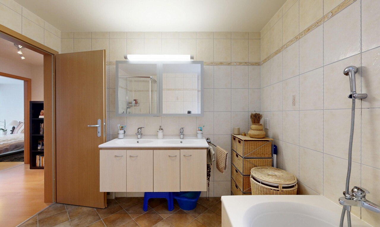 full bathroom with double vanity, tile walls, a tub, and dark tile patterned flooring