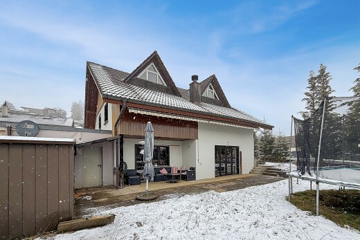 snow covered house with a trampoline, stucco siding, and a chimney