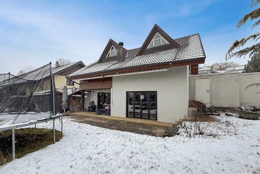 snow covered house featuring a trampoline, a tiled roof, stucco siding, and a gate