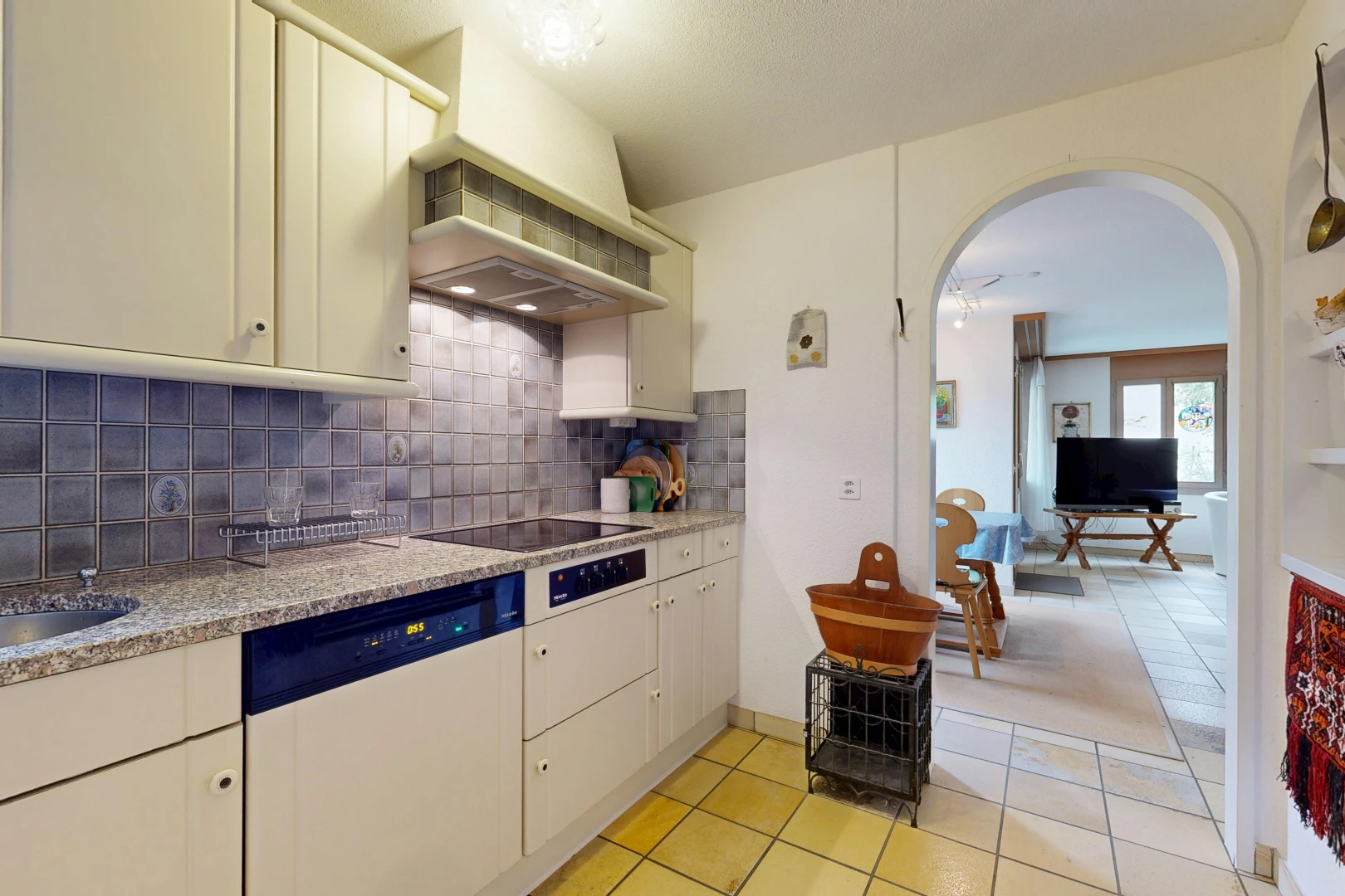 kitchen featuring arched walkways, white dishwasher, light tile patterned floors, and cream cabinetry