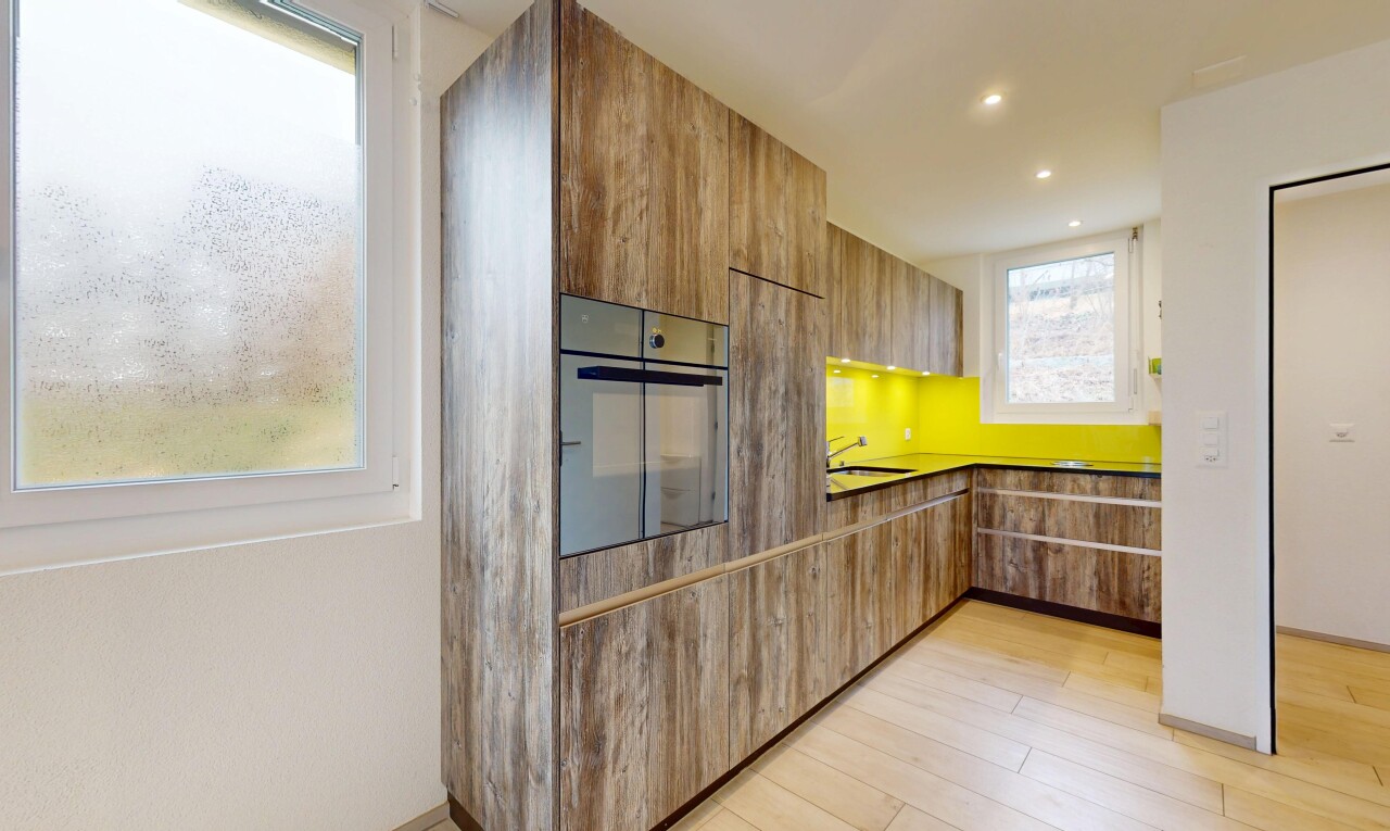 cuisine avec four, lumière naturelle, plans de travail, sol en finition bois, et armoires à panneau plat