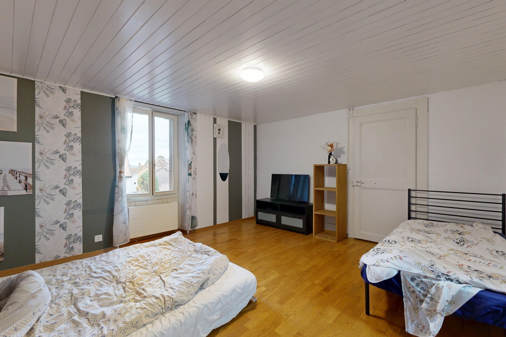 chambre avec sol en finition bois, wood finish floor, télévision, lumière naturelle, et natural light