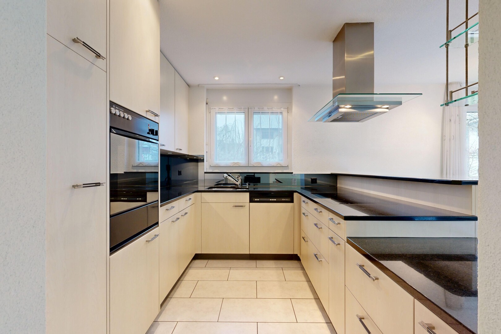 kitchen featuring range hood, oven, dishwasher, light tile patterned floors, and dark stone counters