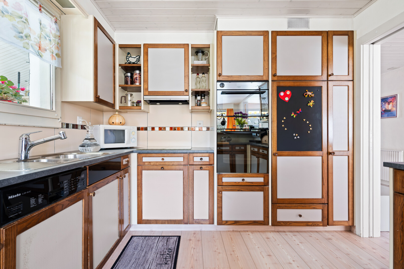 dual tone kitchen with dishwasher, light wood finished floors, two tone cabinets, white microwave, and open shelves