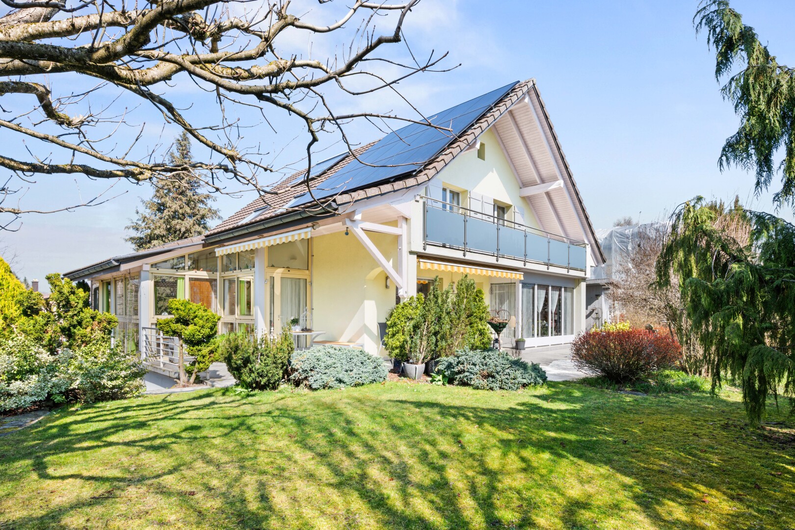 outdoor house featuring a lawn, a balcony, a patio area, solar panels, and stucco siding