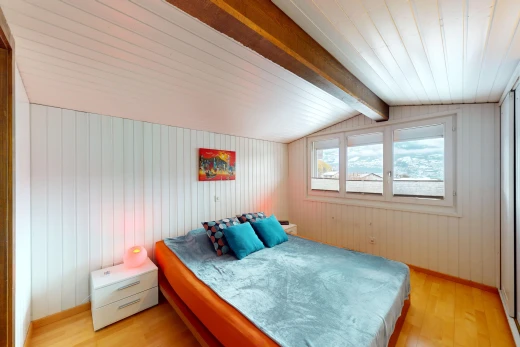 chambre avec mur en bois, plancher de bois, poutres apparentes, plafond voûté, et lumière naturelle