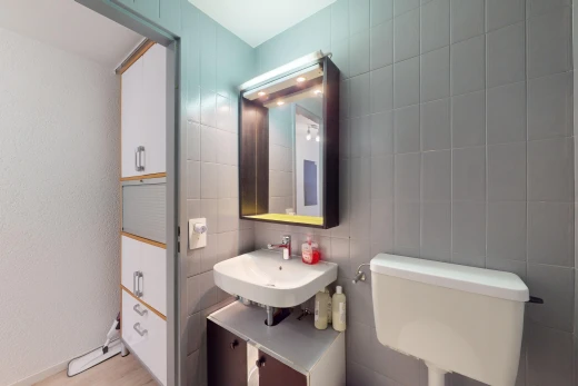salle de bains avec mur carrelé, vasque, toilettes, miroir, et plancher de bois