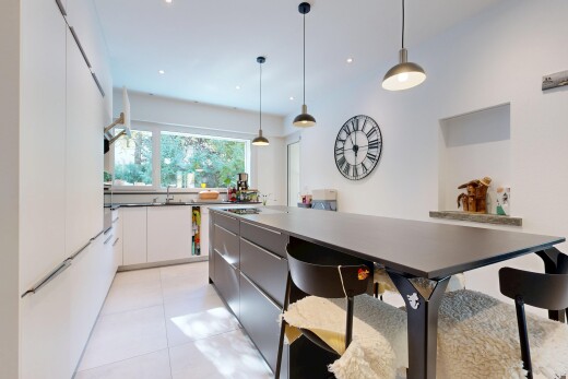dual tone kitchen with hanging light fixtures, two tone cabinetry, modern cabinets, dark countertops, and a kitchen bar