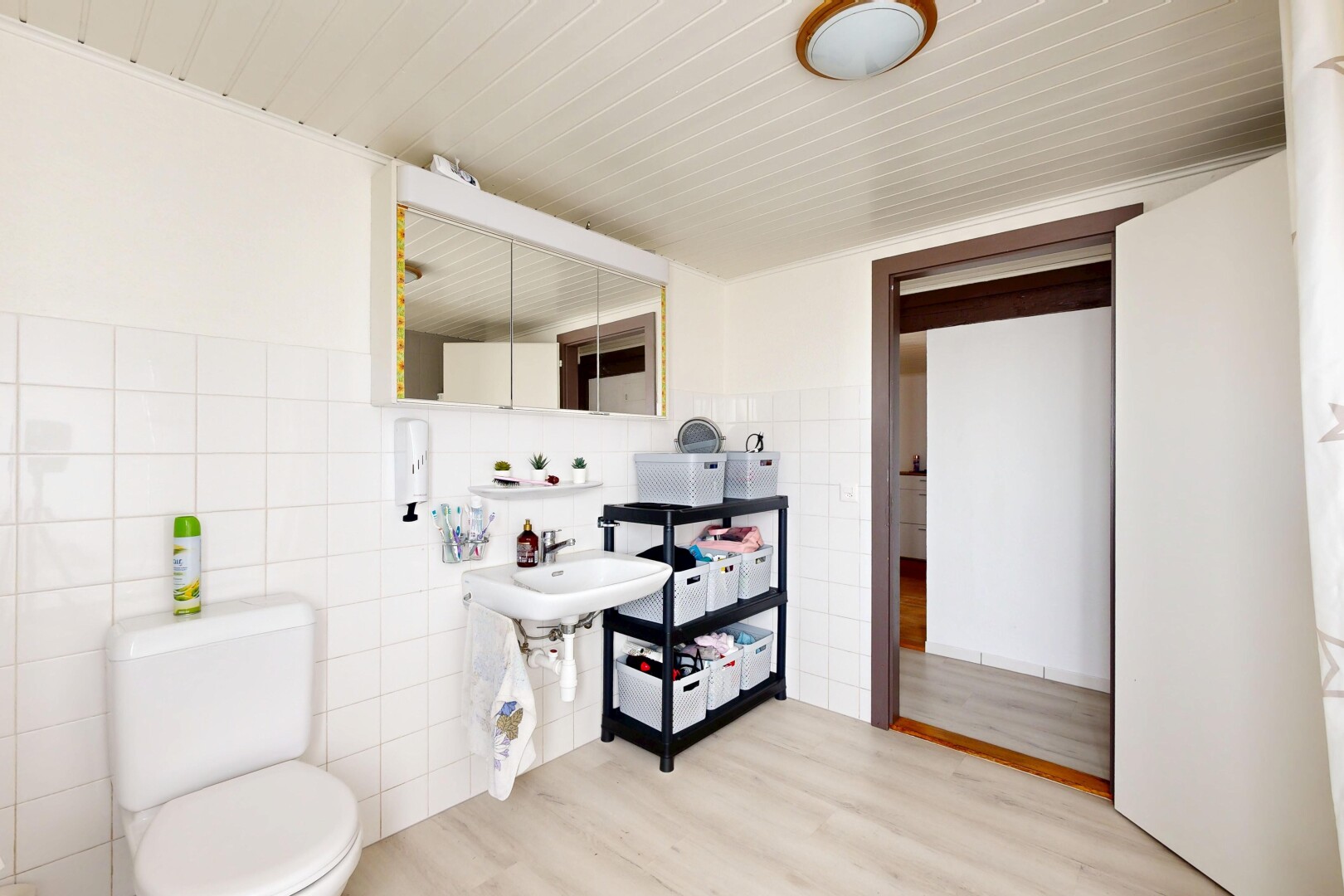 salle de bains avec mur en carrelage, tile wall, miroir, toilette, et sol en finition bois