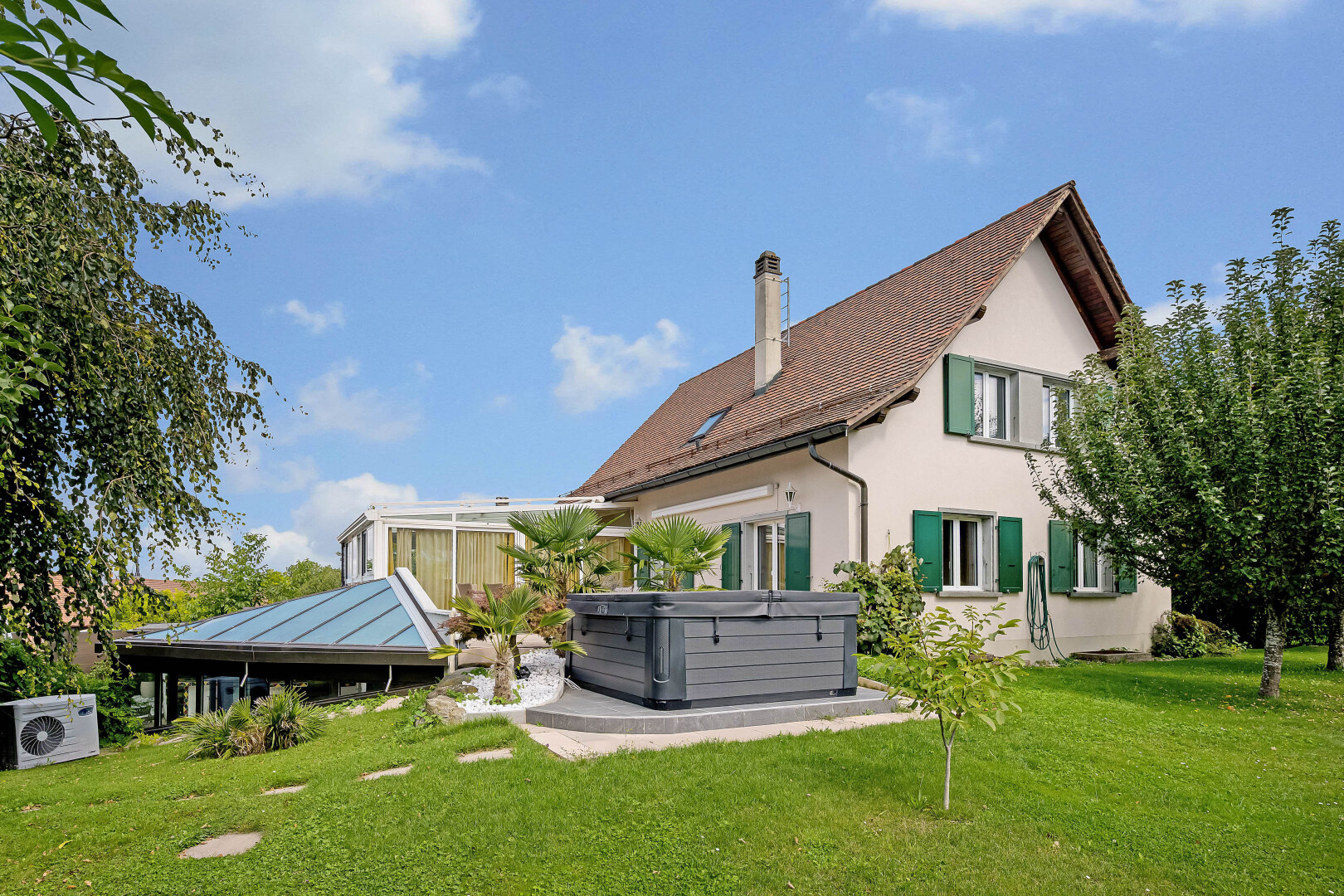 outdoor house featuring a hot tub, a yard, stucco siding, and a chimney