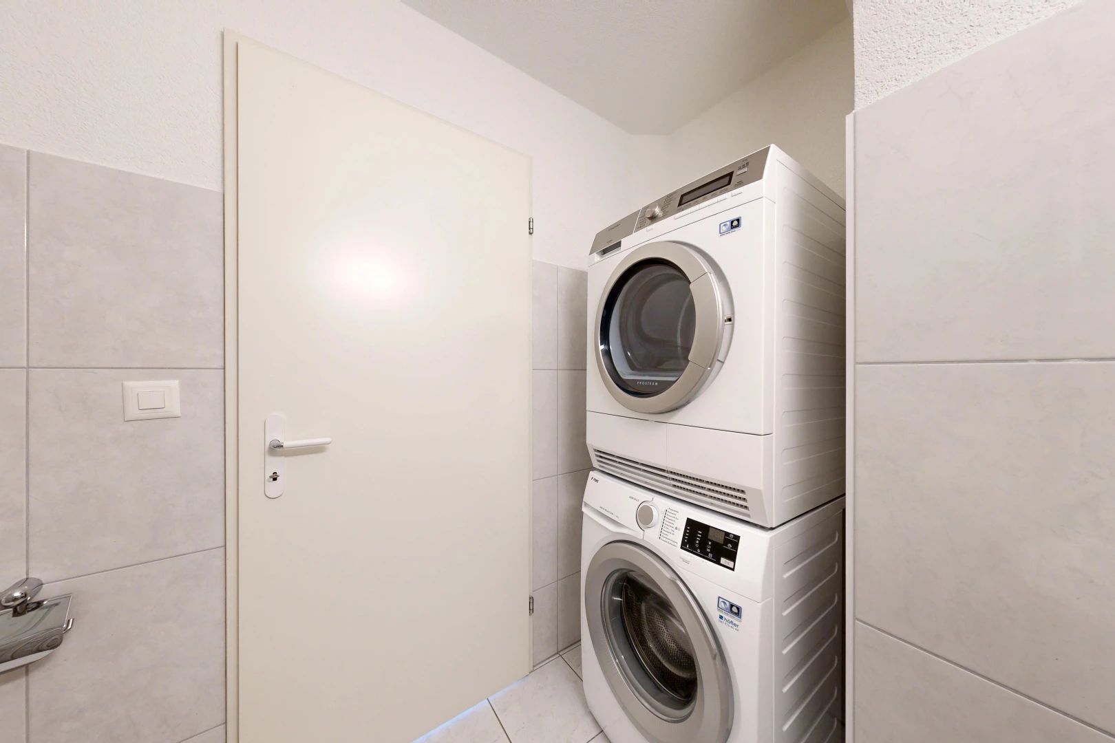 buanderie avec lave-linge et sèche-linge superposés, mur en carrelage, tile wall, sol en carrelage, et tile floor