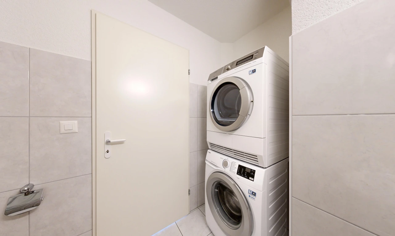 buanderie avec lave-linge et sèche-linge superposés, mur en carrelage, tile wall, sol en carrelage, et tile floor