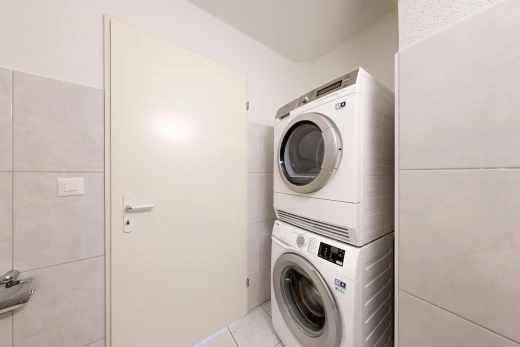 buanderie avec lave-linge et sèche-linge superposés, mur en carrelage, tile wall, sol en carrelage, et tile floor