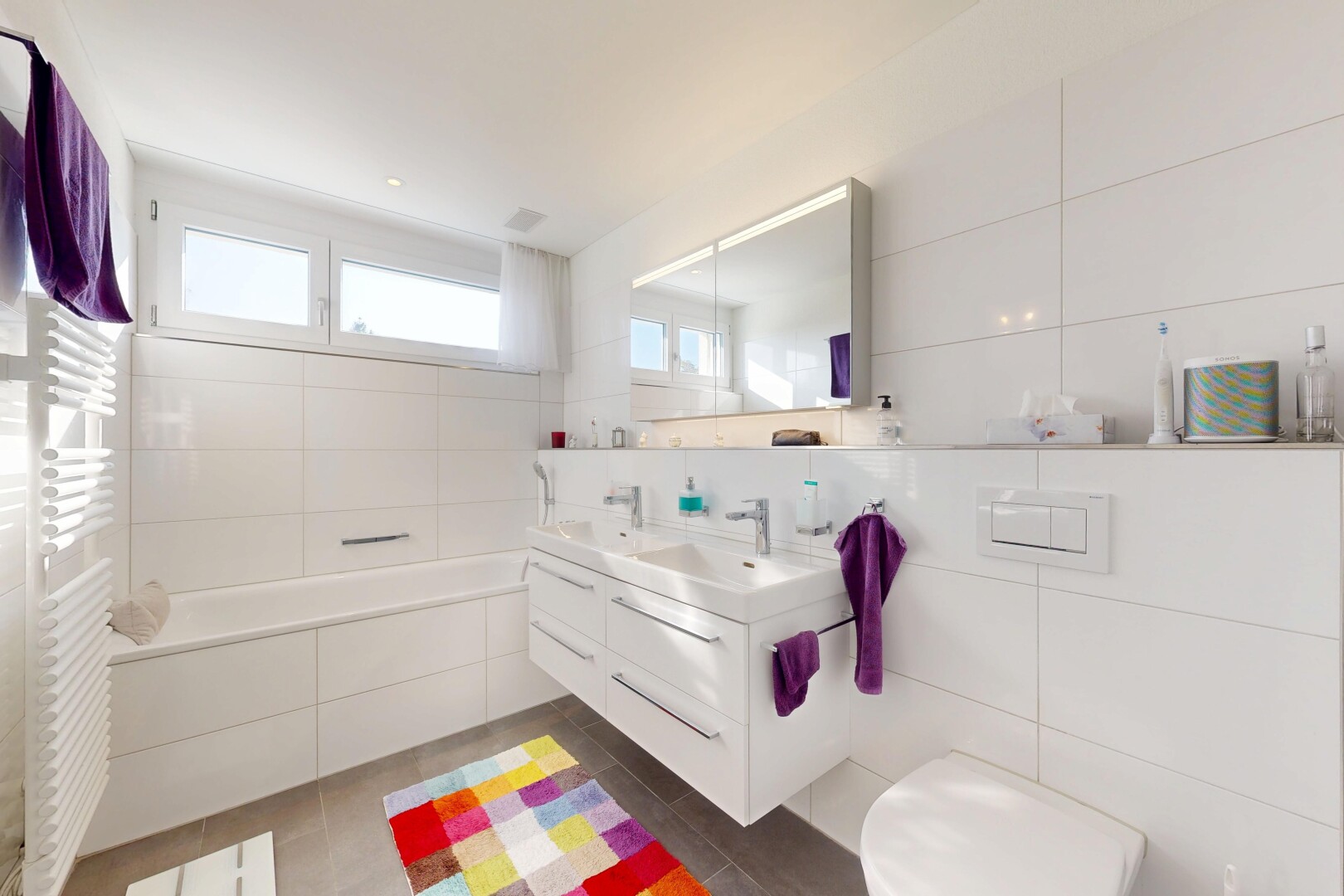 bathroom featuring tile walls, double vanity, a garden tub, radiator, and a towel warming rack