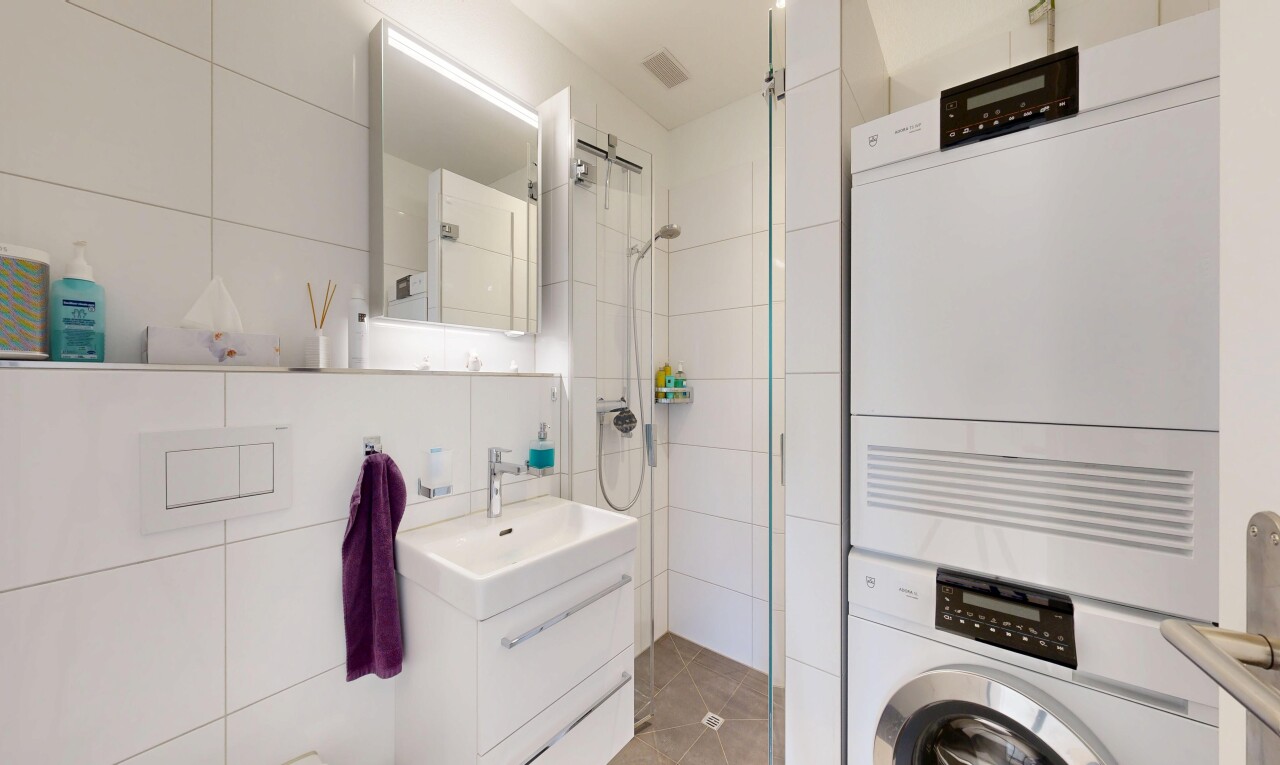bathroom featuring tile walls, vanity, tiled shower, and stacked washing machine and dryer