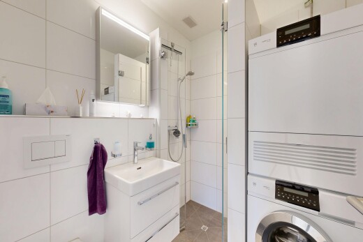 bathroom featuring tile walls, vanity, tiled shower, and stacked washing machine and dryer