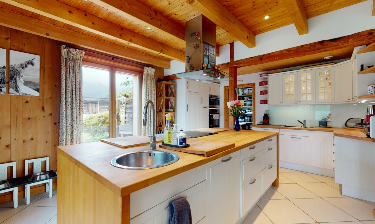 cuisine avec îlot de cuisine, poutres apparentes, meubles vitrés, et plan de travail en bois