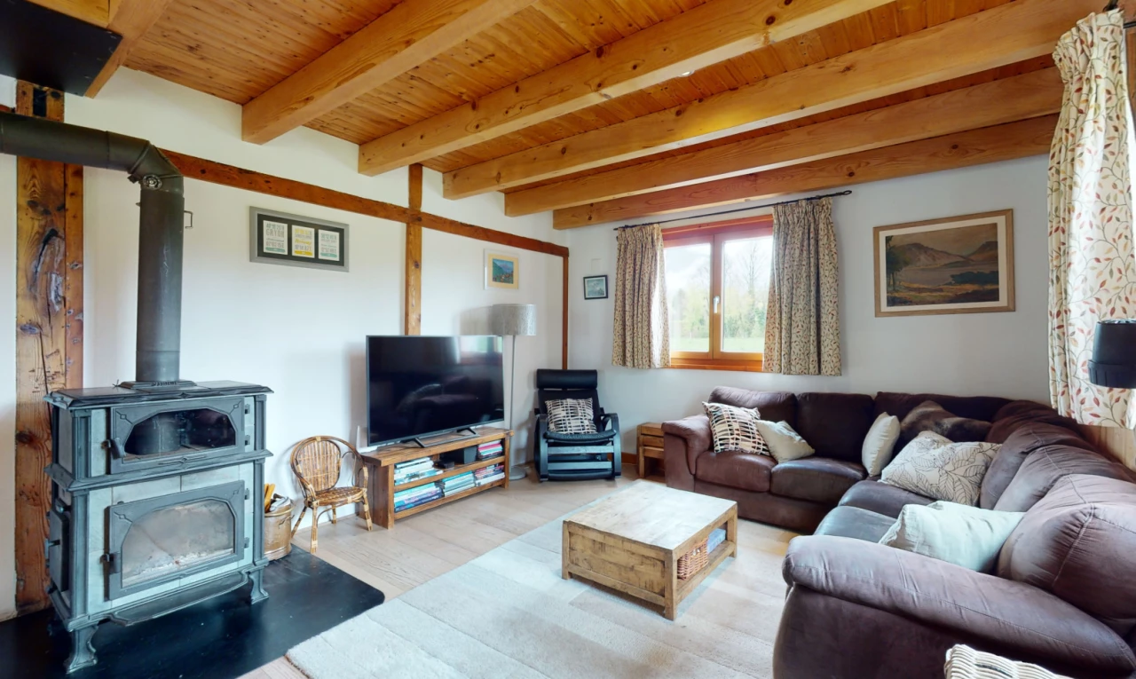 salon avec télévision, plafond de bois, lumière naturelle, poutres apparentes, et poêle à bois