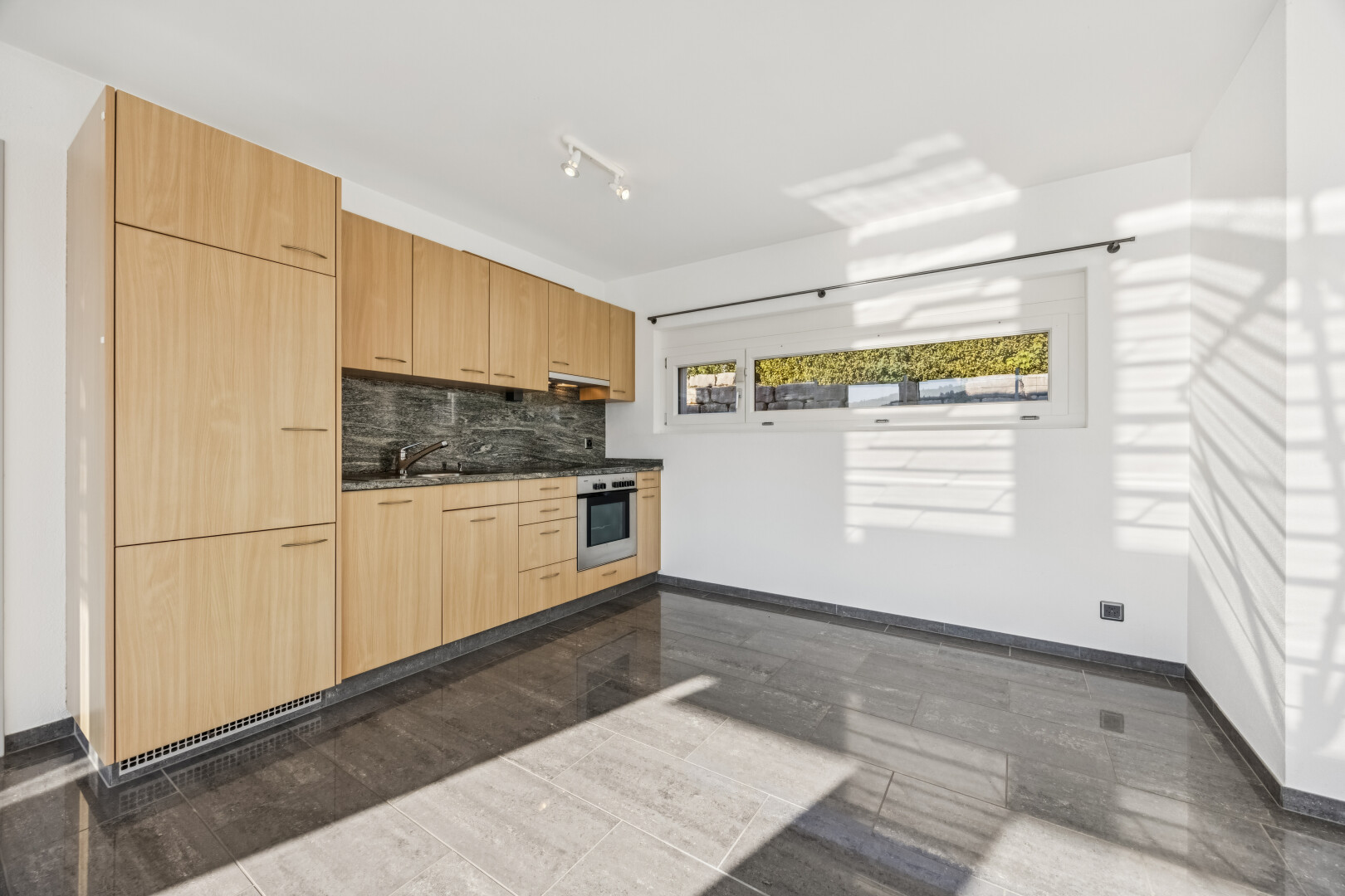 küche mit deckenbeleuchtung, dark countertops, light brown cabinets, hellbraune schränke, und flat panel cabinets