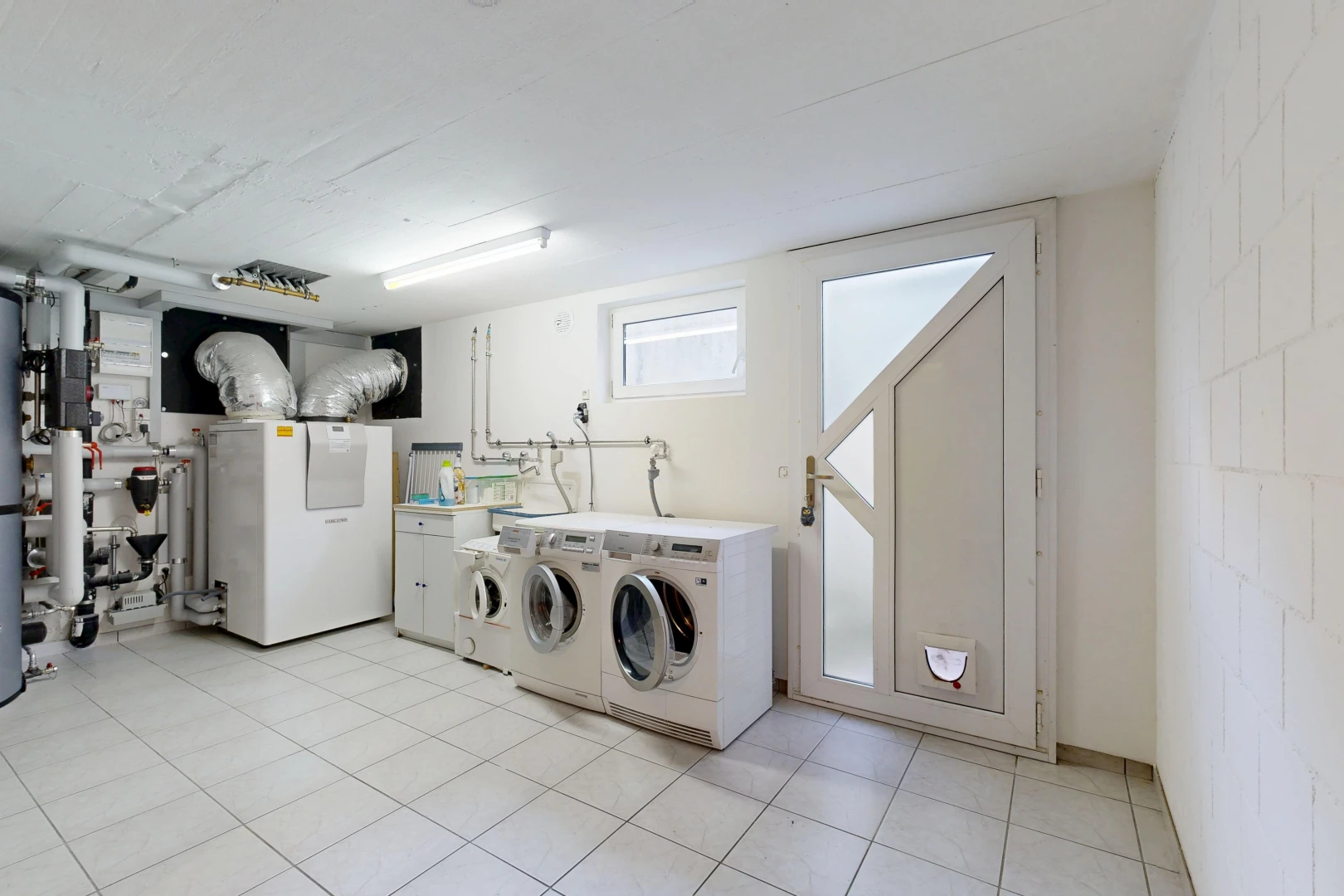 laundry room with washing machine and clothes dryer, concrete block wall, light tile patterned flooring, and heating unit