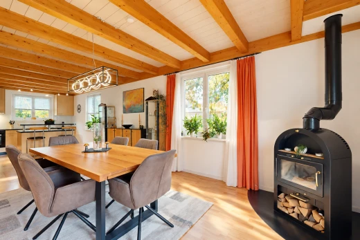 dining room featuring a wood stove, light wood finished floors, and a wood ceiling with exposed beams