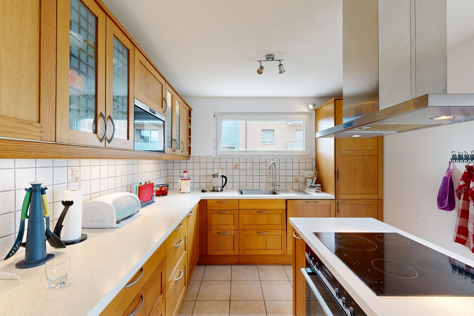 cuisine avec hotte, backsplash, dosseret, light countertops, et armoires marron moyen