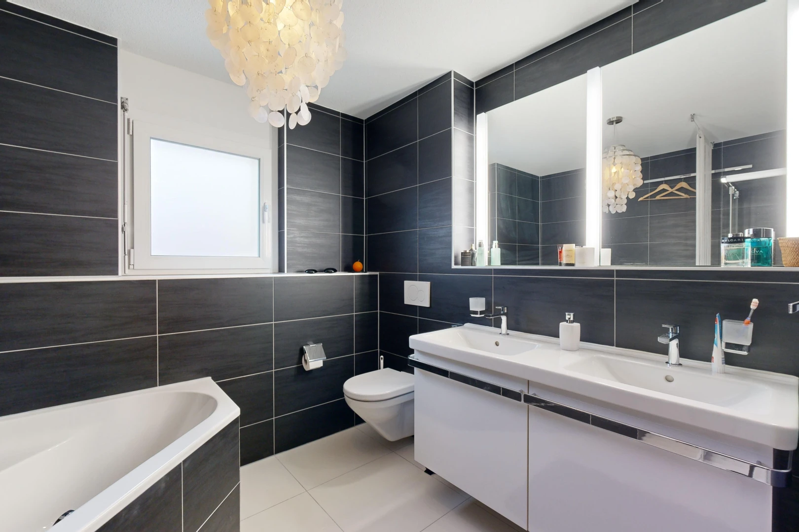 bathroom featuring vanity, tiled tub, an inviting chandelier, tile walls, and tile patterned flooring
