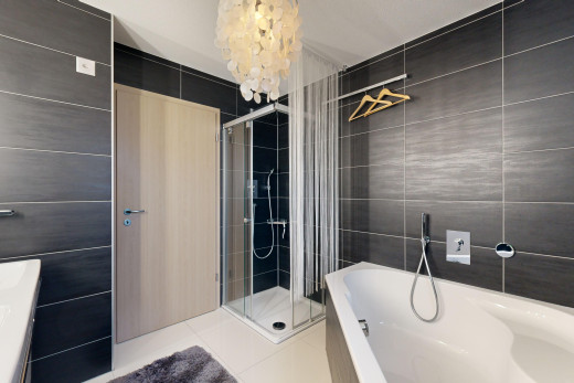 salle de bains avec carrelage, douche, baignoire, lustre, et mur carrelé