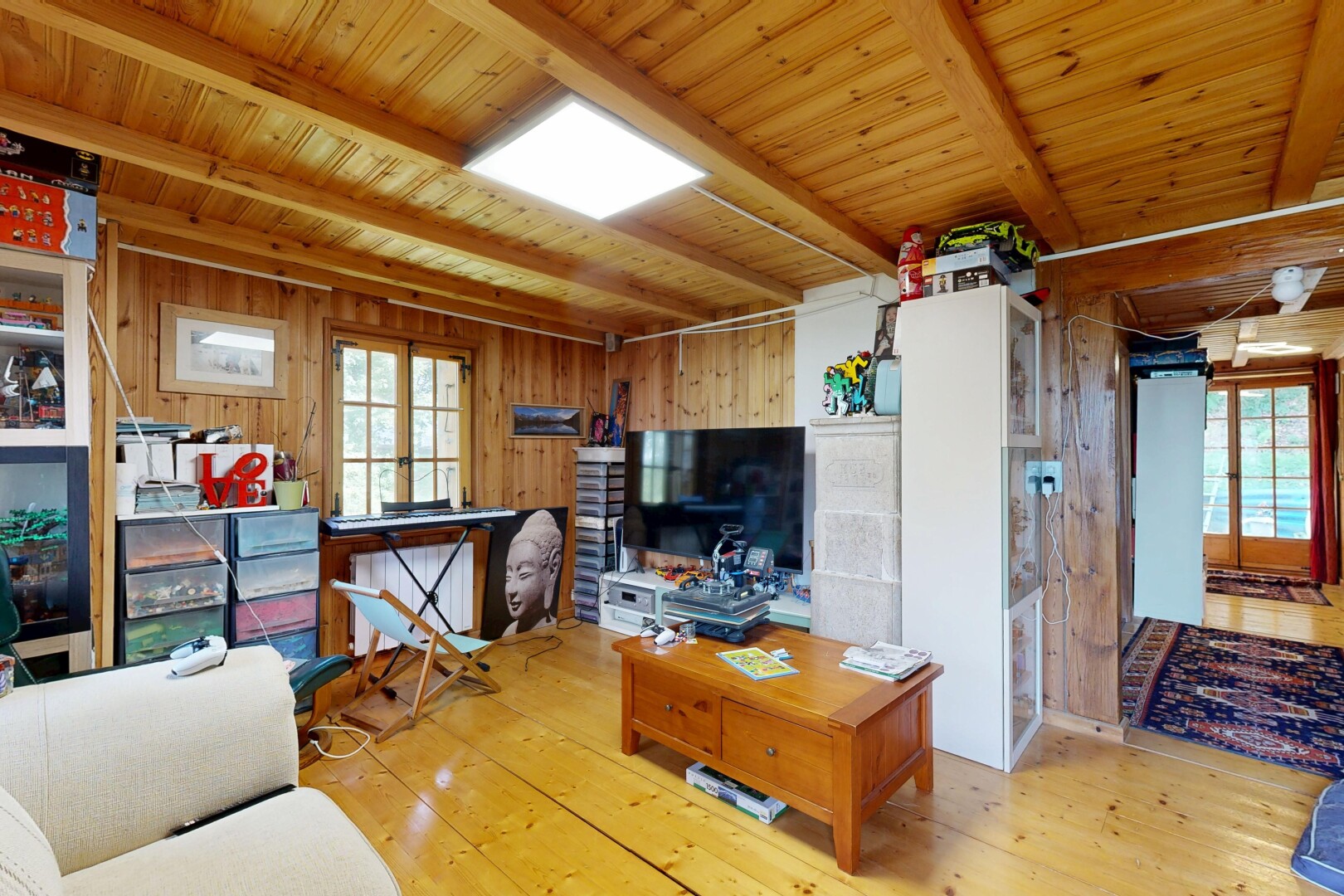 salon avec plafond à poutres, beamed ceiling, portes-fenêtres, dated wood wall, et télévision