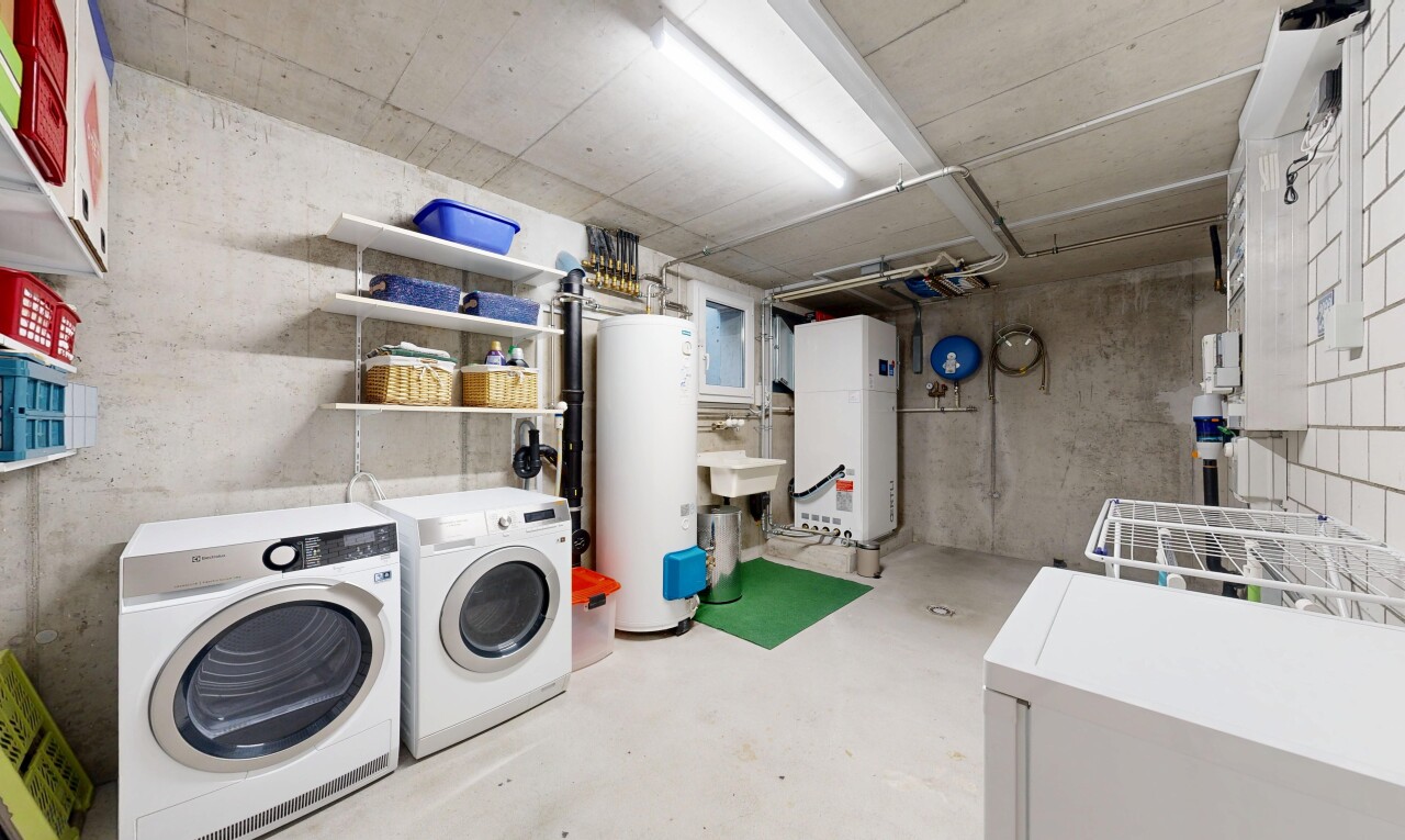 buanderie avec mur en béton, concrete wall, chauffe-eau, sol en béton, et concrete floor