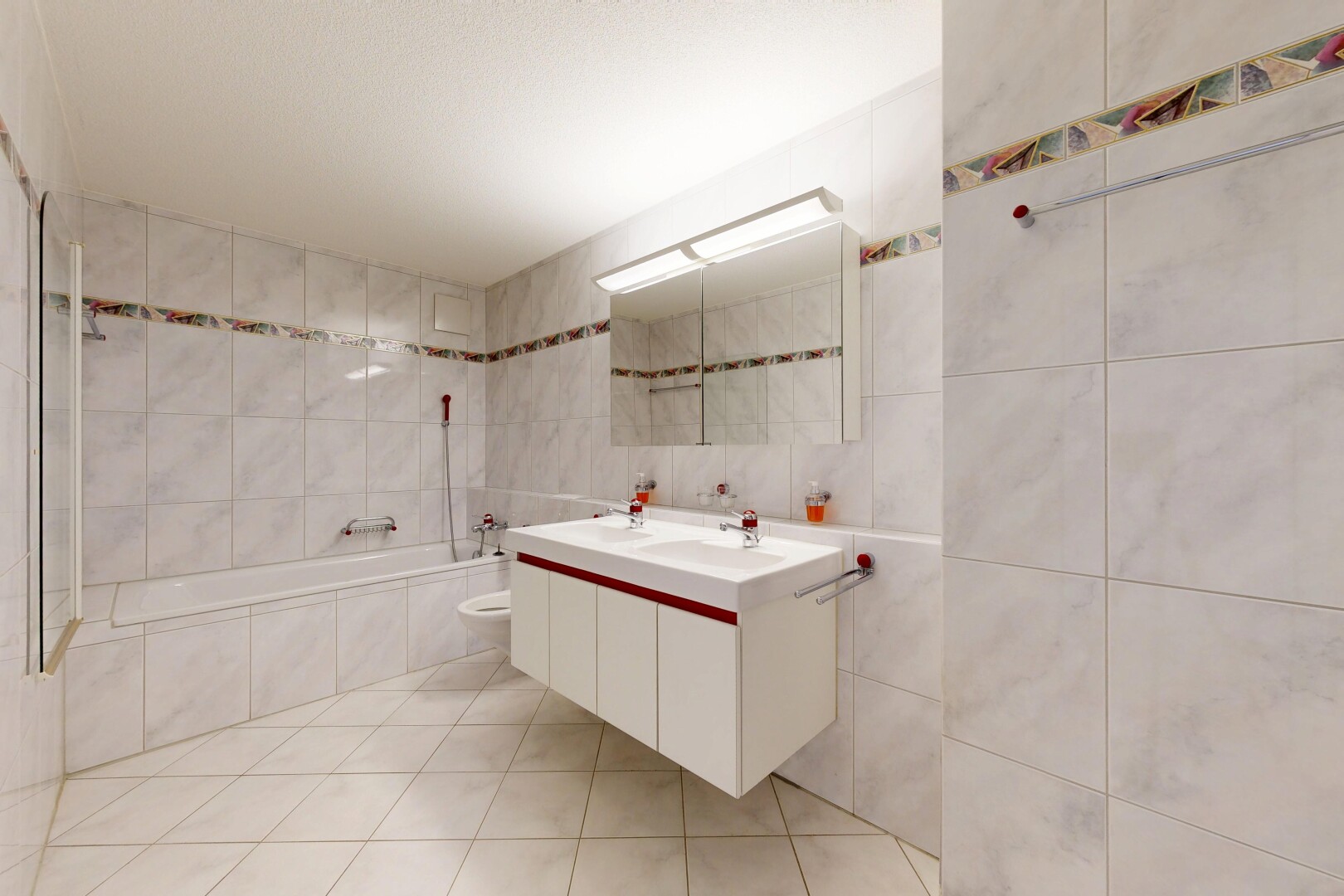 salle de bains avec salle de bain complète, double vasque, light floor, miroir, et mur en carrelage
