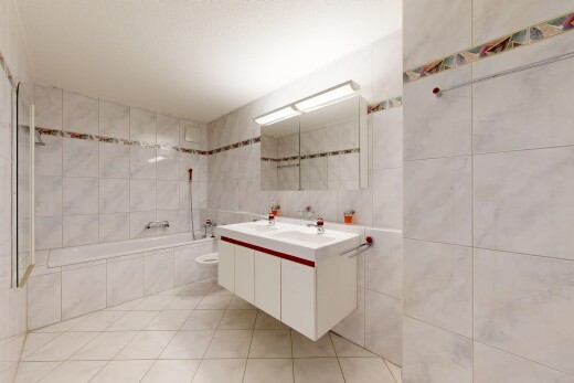 salle de bains avec salle de bain complète, double vasque, light floor, miroir, et mur en carrelage