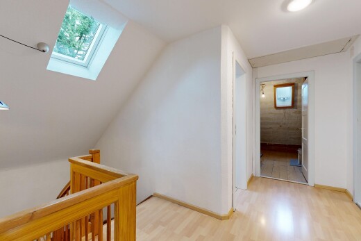 hall with light wood finished floors, a skylight, and an upstairs landing
