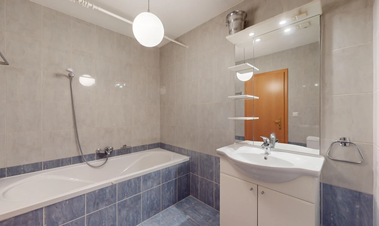 salle de bains avec bain-douche, mur carrelé, miroir, et meuble-lavabo