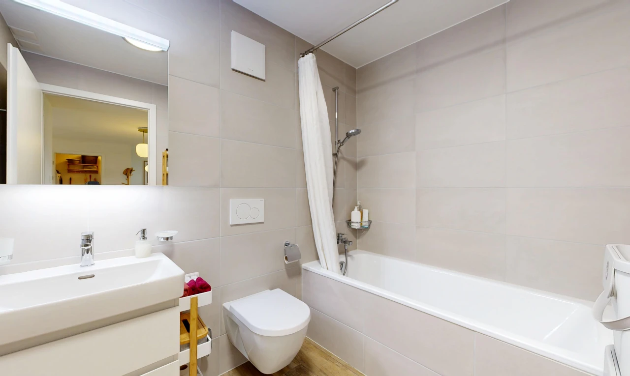 salle de bains avec douche-bain combinés, salle de bain complète, miroir, lavabo (ou coiffeuse selon le contexte), et mur en carrelage