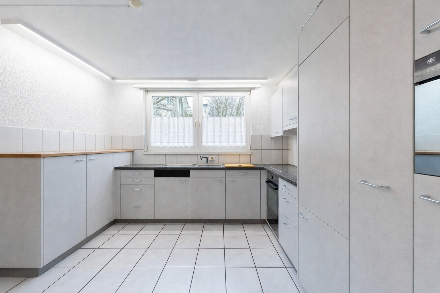 kitchen featuring dark countertops, dishwasher, oven, white cabinetry, and light tile patterned floors