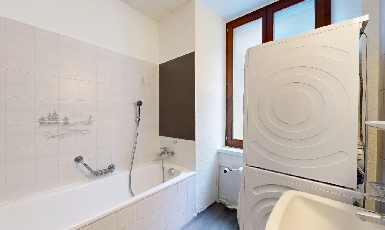 bathroom featuring tiled tub and stacked washer / drying machine